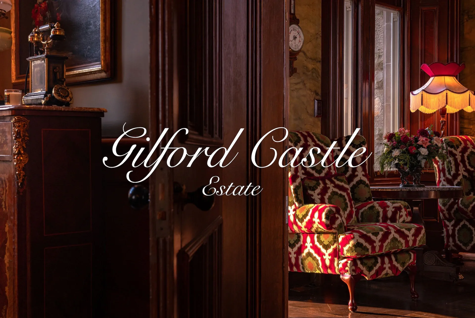 The Gilford Castle Estate script wordmark in white over a lamplit drawing room with wood panelling, an antique clock and red patterned armchairs.