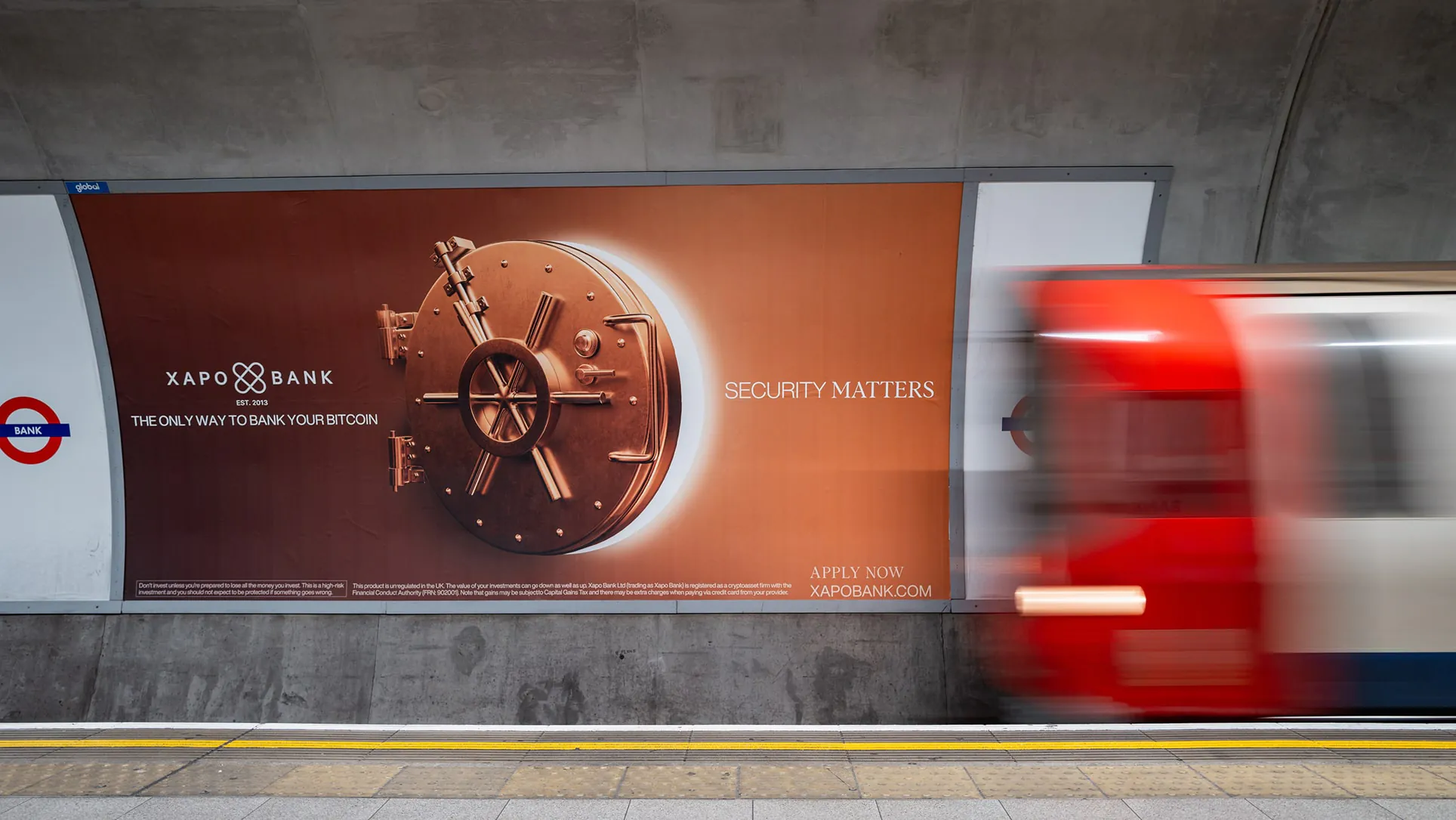 A London Underground platform poster shows a copper vault door and “Security Matters” as a red train blurs past.